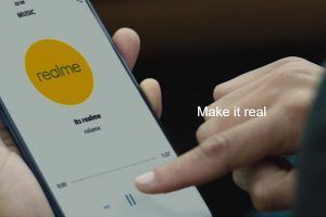 smartphone con logo Realme e in sovrapposizione il nuovo slogan 'Make it Real'.